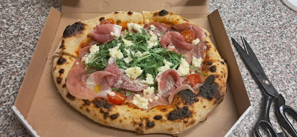 Frissen sült nápolyi pizza a kiszállítási dobozban, prosciuttóval és rukkolával