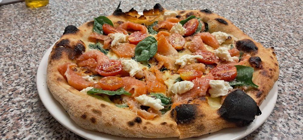 Kemencében sült nápolyi pizza fehér tányéron, koktélparadicsommal és bébispenóttal